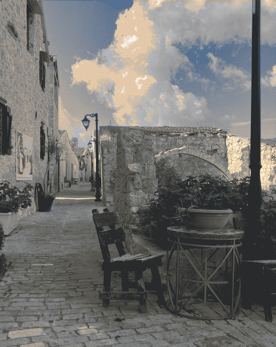 A small stone road in a village with houses and a chair in the foreground.