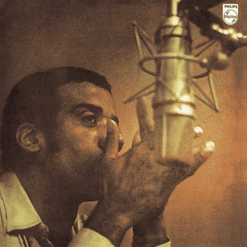 Afro-Brazilian musician Jorge Ben Jor clapping his hands over his mouth in the background, partly obscured by a recording mic in the foreground.