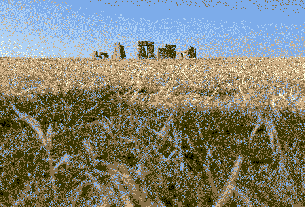Clear blue sky with Stonehenge small in the distance and yellow grass close up.
