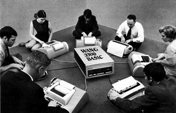 People sitting in a circle typing on typewriters, connected to the same computer.